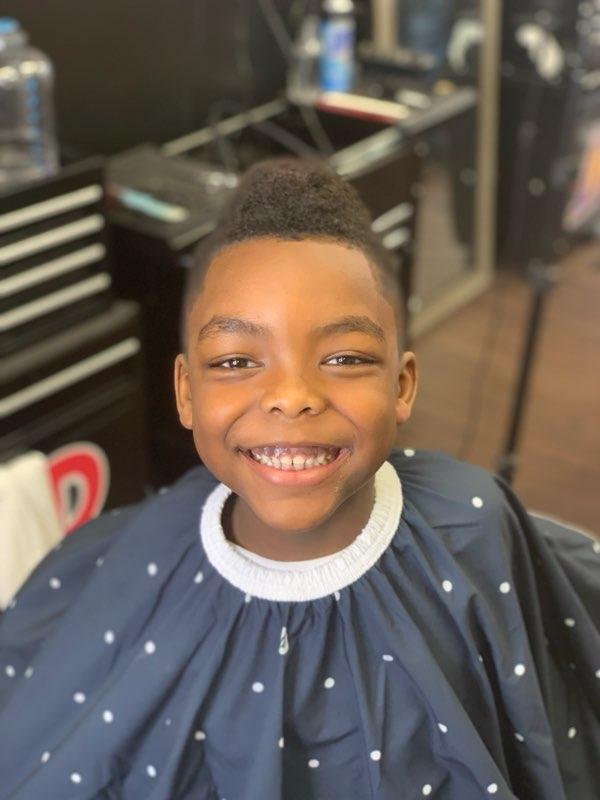 a smiling kid wearing a dotted cape after a haircut, surrounded by grooming items